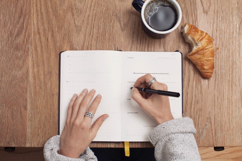 Una autónoma escribiendo en su libreta mientras toma café las diferencias entre actividades empresariales y profesionales